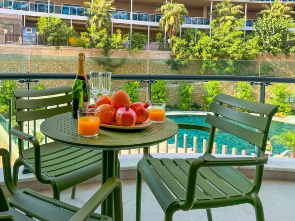 Un balcon avec une table préparée pour le petit-déjeuner, comprenant une bouteille de champagne, des verres, des oranges, des grenades et un verre de jus d’orange.