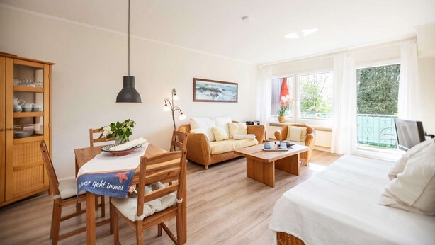 Habitación luminosa con una mesa de comedor de madera, sillas, un sofá, una cama y una ventana que ofrece vistas a zonas verdes.