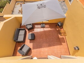 Una terraza en la azotea con mobiliario exterior, una parrilla y un gran paraguas.