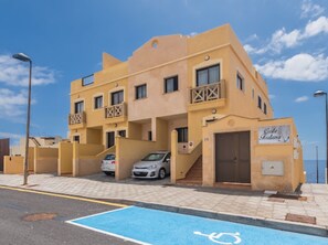 Un edificio de varios pisos con balcones, un estacionamiento y un letrero que indica un restaurante.
