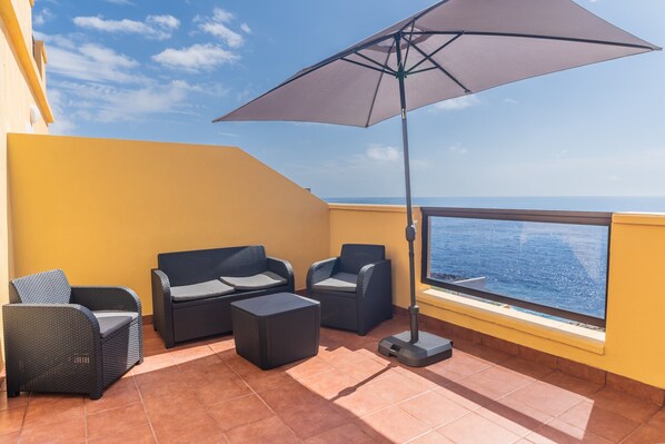 Un balcón con mobiliario exterior, una sombrilla grande y vista al mar.