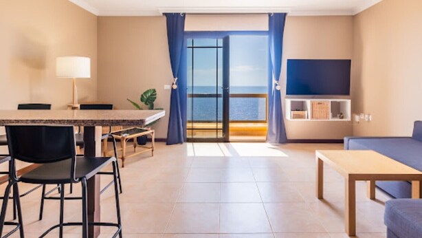 Et moderne værelse med spiseplads, sofa, tv og en balkon med udsigt.
