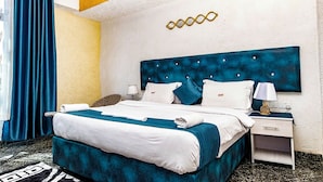 A hotel room with a large bed, white bedding, a blue headboard, a nightstand with a lamp, and a curtain. - Nur Complex Hotel  (Nairobi)