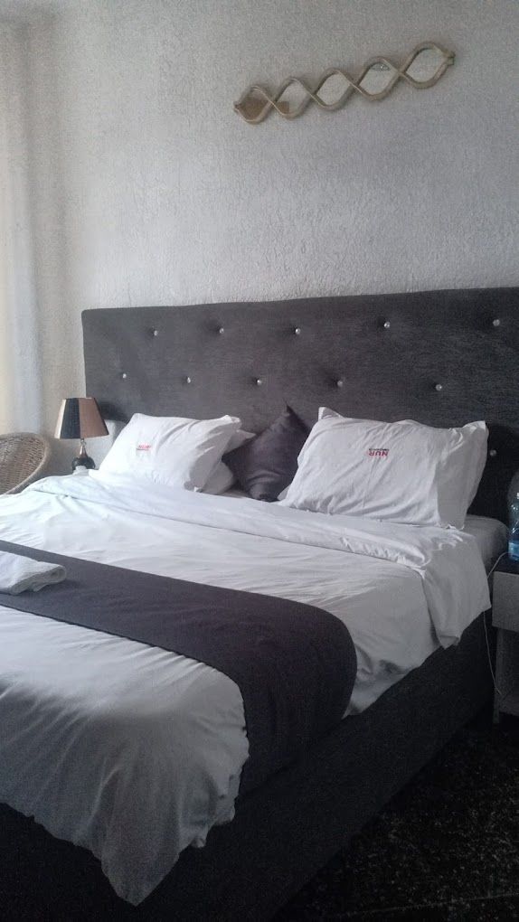 A neatly made bed with white and dark bedding, a headboard with a decorative pattern, and a lamp on the side.