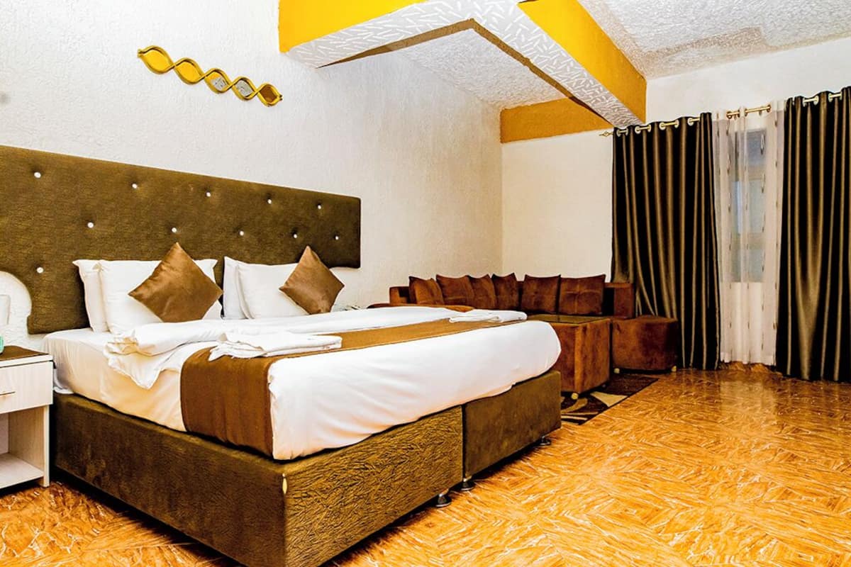 A hotel room with a large bed, a wooden headboard, a nightstand, and a curtain.