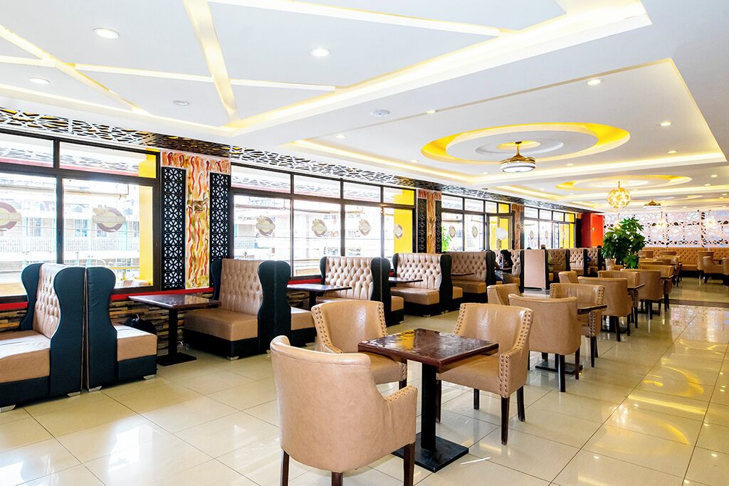 A restaurant with booths and tables, a patterned ceiling, and large windows.