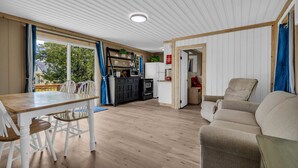 Un espace de vie et de salle à manger moderne, à plan ouvert, avec un plancher en bois, des murs blancs et une cuisine à l’arrière-plan.