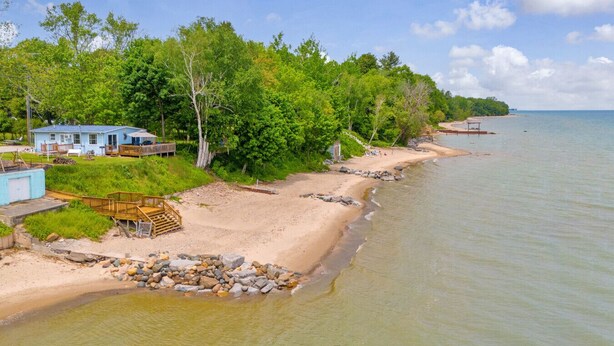 Une propriété située en bord de mer, comprenant une petite maison, une terrasse en bois et une plage de sable.