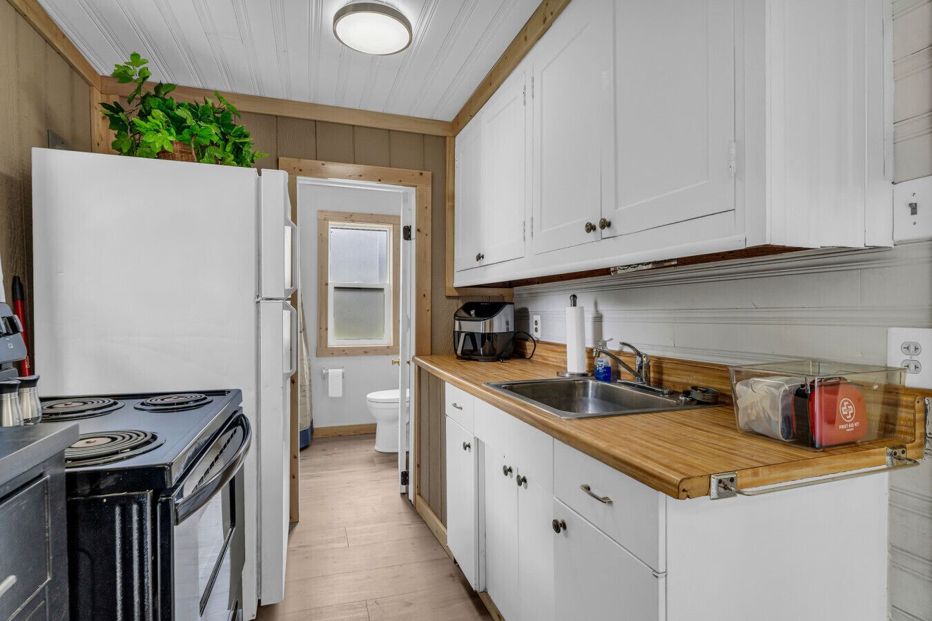 Una cocina compacta con gabinetes blancos, una encimera de madera, una estufa y un lavabo.