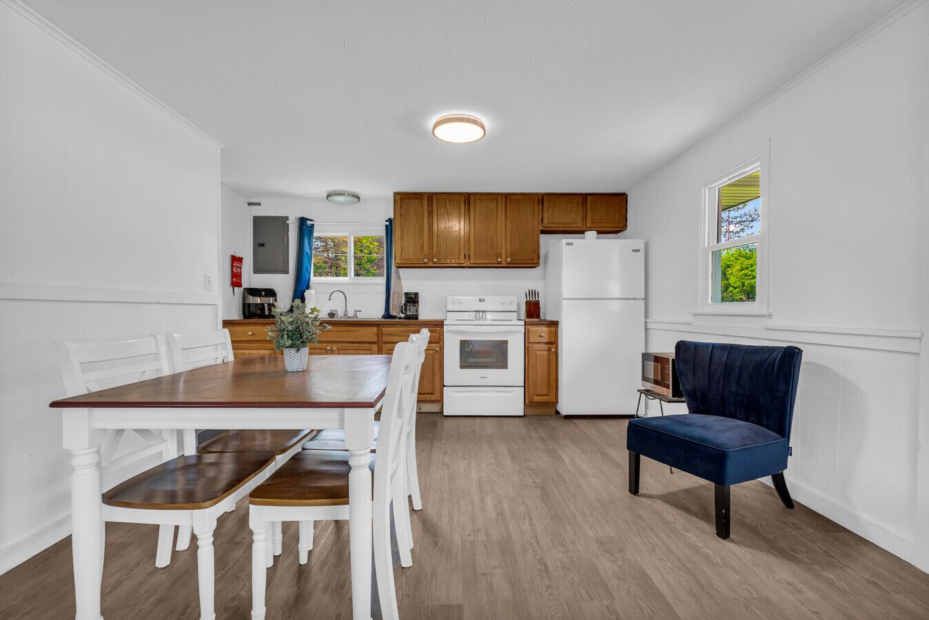 A modern kitchen with wooden cabinets, a white refrigerator, and a dining area with a wooden table and white chairs.