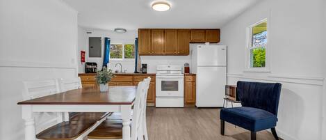 A modern kitchen with wooden cabinets, a white refrigerator, and a dining area with a wooden table and white chairs.