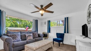 A living room with a grey sofa, a blue chair, a wooden floor, and a ceiling fan. - North Bound 25 Cottage #3 (Lexington)