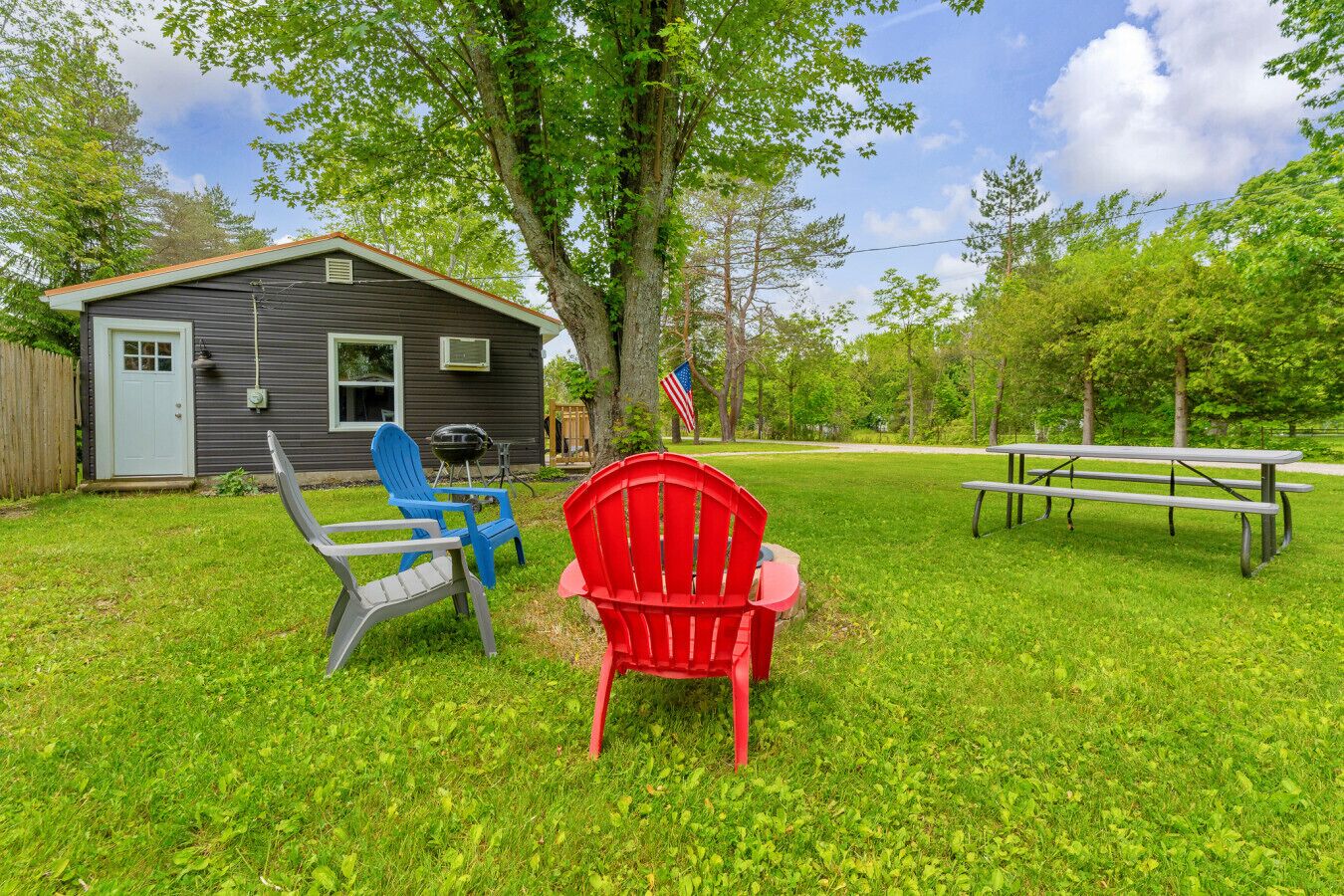 A backyard with a house, a barbecue grill, outdoor chairs, and a picnic table.