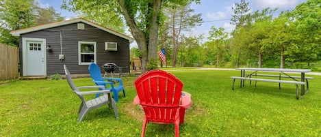 A backyard with a house, a barbecue grill, outdoor chairs, and a picnic table.