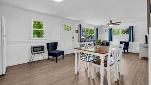 A dining area with a wooden table and white chairs, a ceiling fan, and a television on a stand. - North Bound 25 Cottage #3 (Lexington)