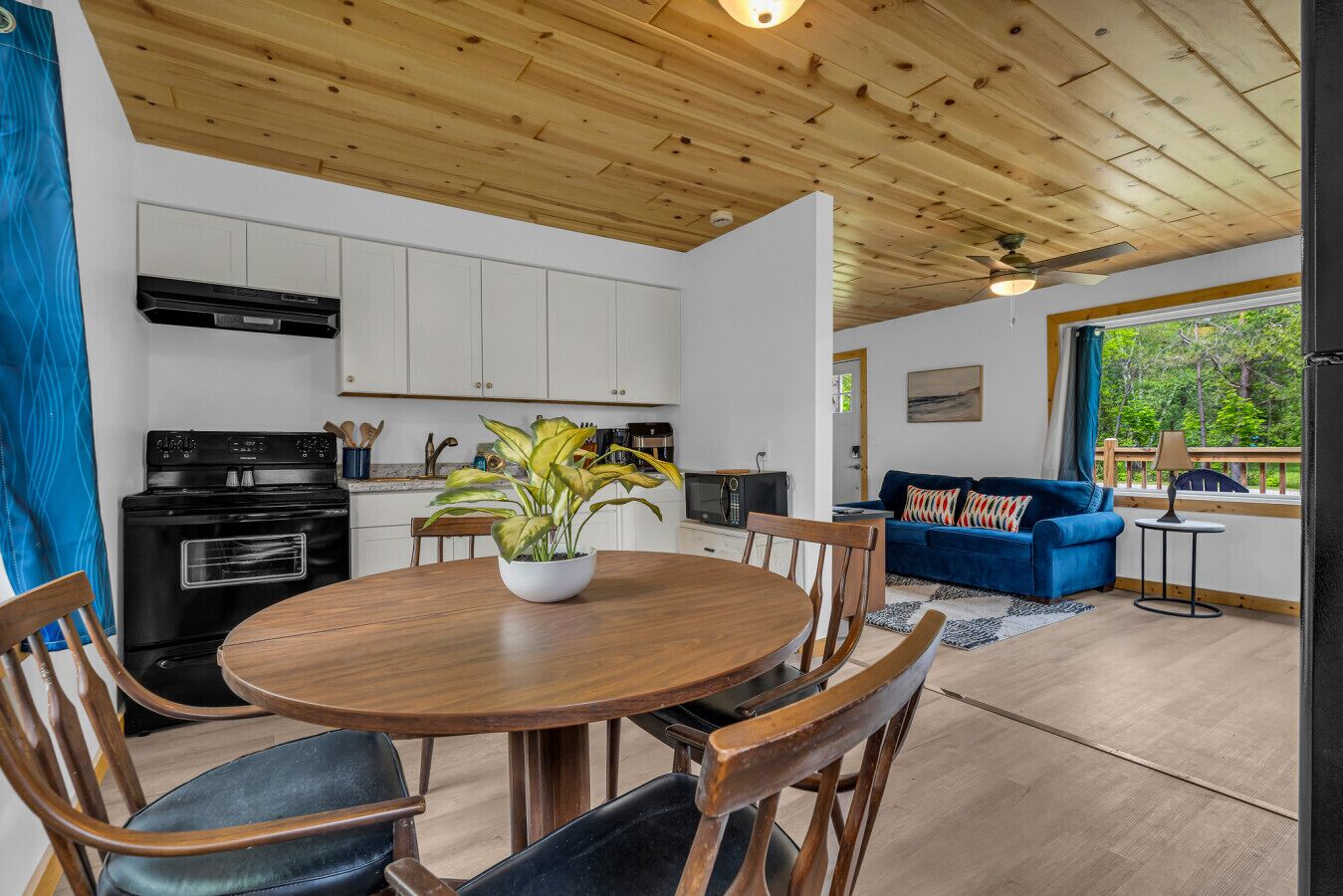 Une cuisine moderne avec des meubles blancs, une cuisinière noire et un coin repas comprenant une table et des chaises en bois.