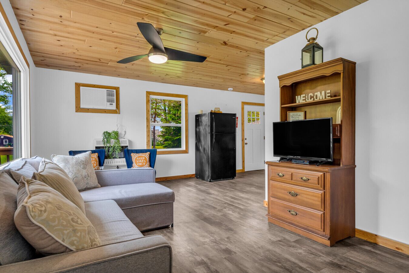 Ein Wohnzimmer mit Sofa, Fernsehschrank, Deckenventilator und Blick ins Freie.