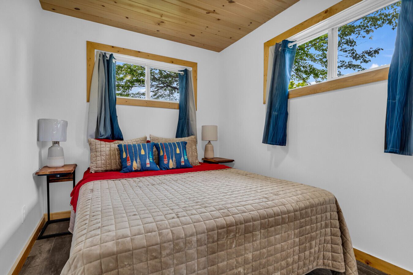 Une chambre à coucher avec un lit, deux tables de chevet, une fenêtre avec des rideaux et un plafond en bois.