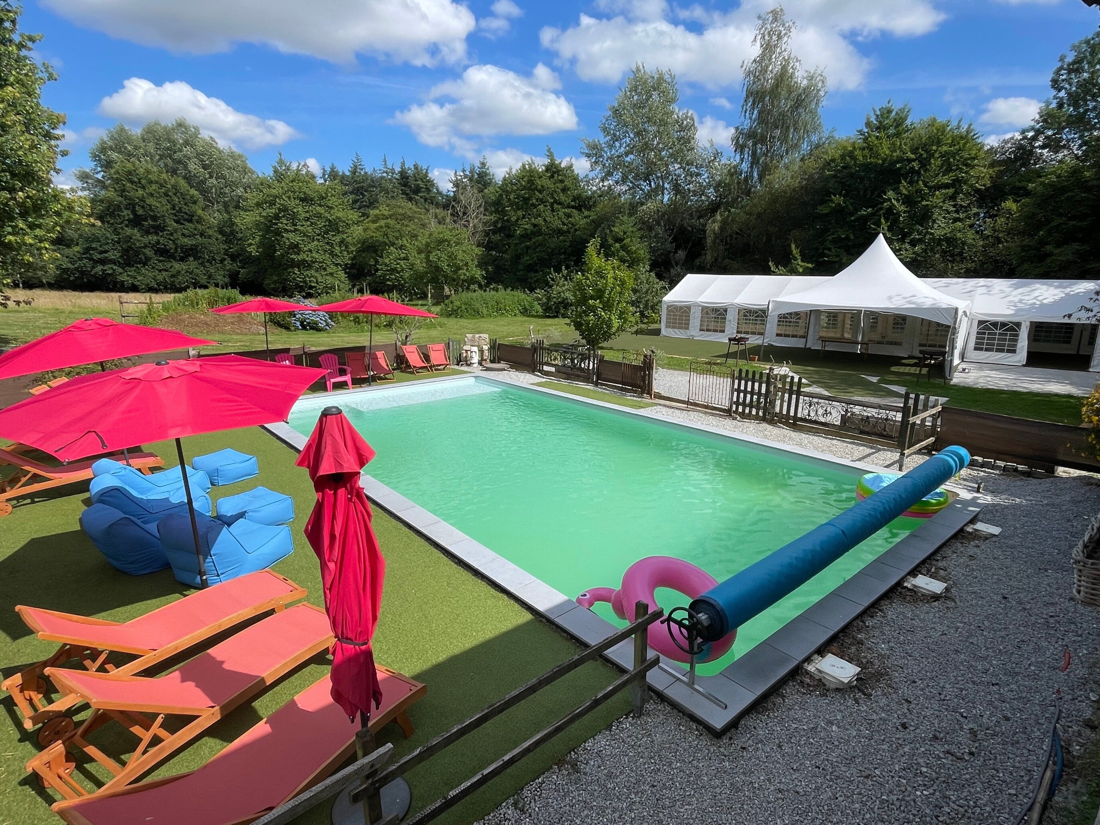 A swimming pool with lounge chairs and umbrellas, surrounded by a fence and trees.