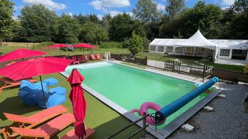 A swimming pool with lounge chairs and umbrellas, surrounded by a fence and trees.