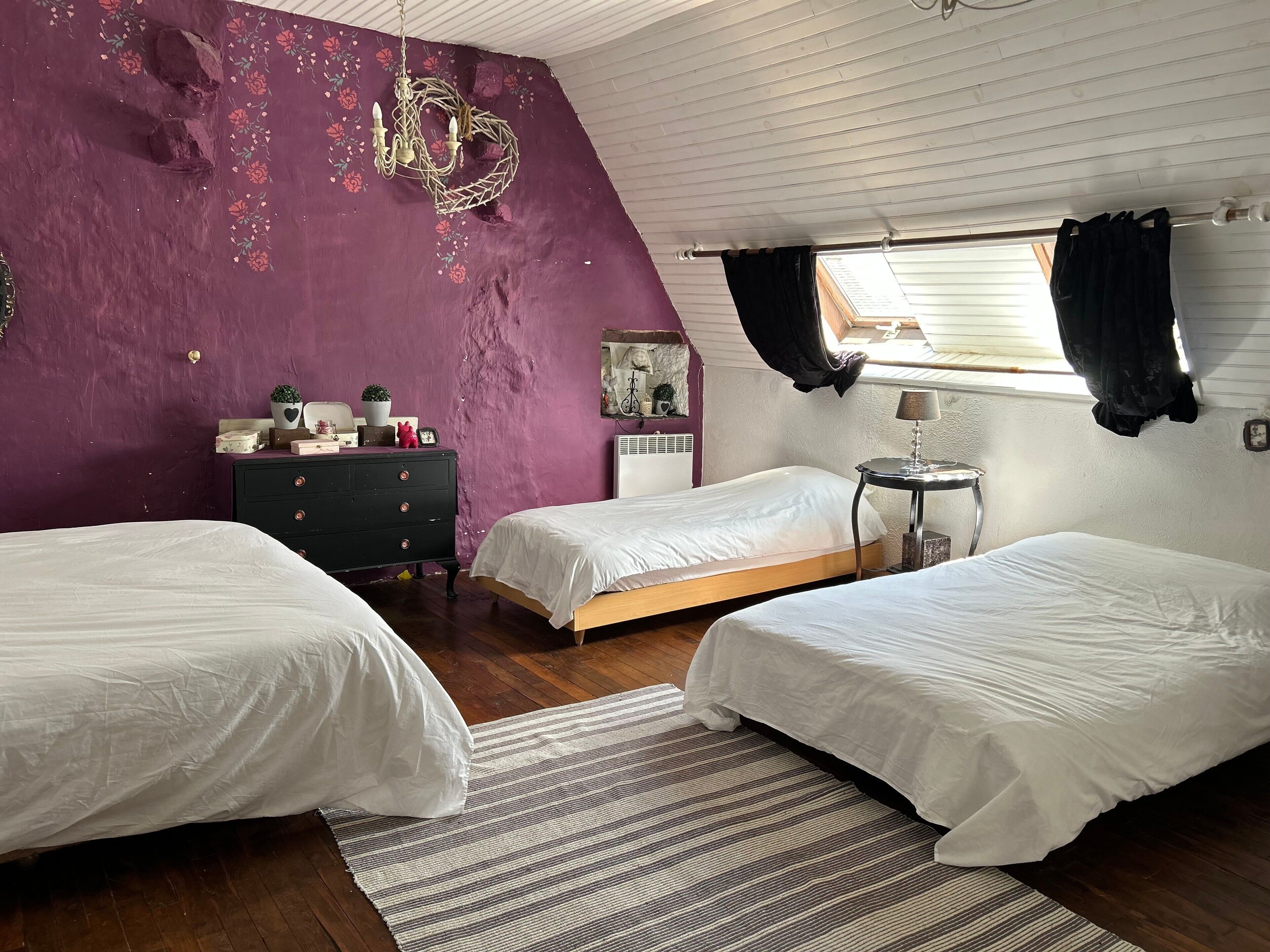 A bedroom with two beds, a dresser, a small table, a window with curtains, and a decorative wall piece.