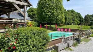 A wooden building with a balcony, a swimming pool, and a large tree in the background. - Complete Domaine Les Hiboux with Heated Pool and Reception Hall (Cléguérec)