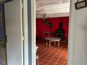A room with a red wall, a tiled floor, a wooden table, a hanging light fixture, and a fireplace. - Complete Domaine Les Hiboux with Heated Pool and Reception Hall (Cléguérec)
