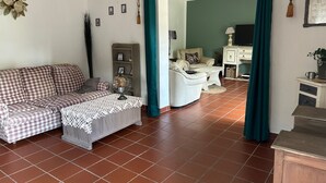 A living room with a checkered sofa, a white armchair, a small table with a globe, and a green curtain. - Complete Domaine Les Hiboux with Heated Pool and Reception Hall (Cléguérec)