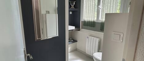 Ein Badezimmer mit Toilette, Radiator, Spiegel und Fenster mit gemusterten Vorhängen.