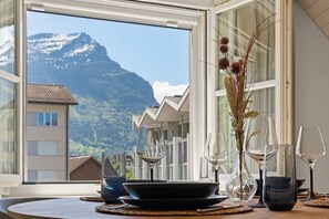 A dining table with wine glasses and a vase of dried plants, set against a mountain view. - AlpsView Jade/FreeParking/AC/Andermatt/Lucerne (Altdorf)