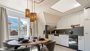 A modern kitchen with white cabinets, a wooden dining table, and pendant lighting. - AlpsView Jade/FreeParking/AC/Andermatt/Lucerne (Altdorf)