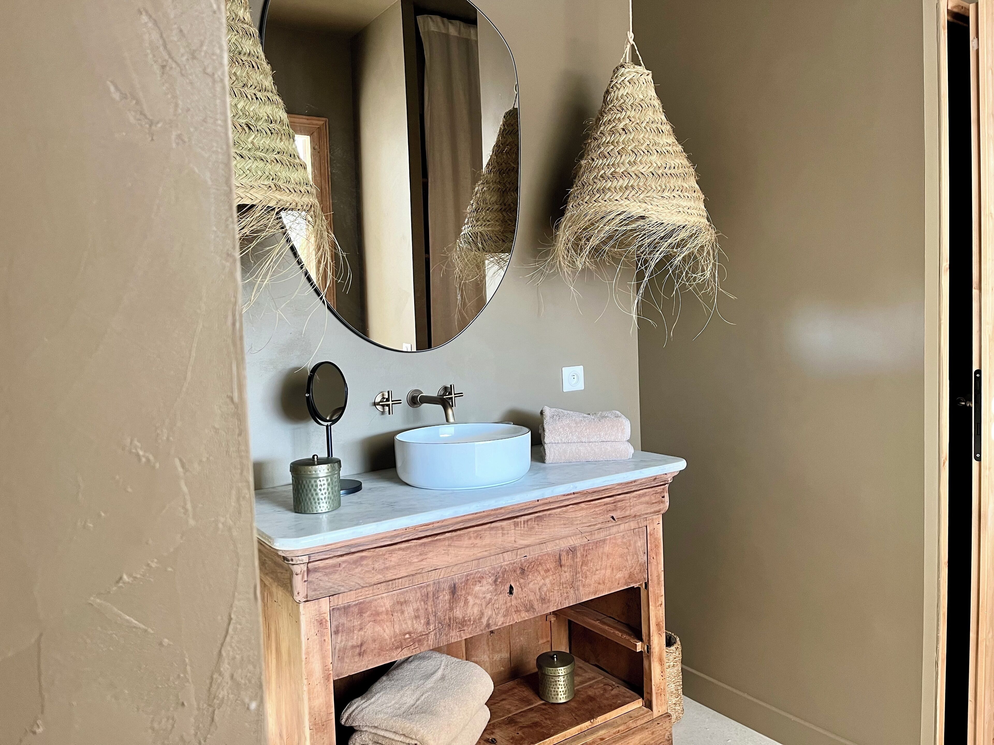 A bathroom with a wooden vanity, a white sink, a round mirror, and two hanging lamps.