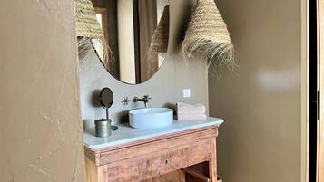 A bathroom with a wooden vanity, a white sink, a round mirror, and two hanging lamps.