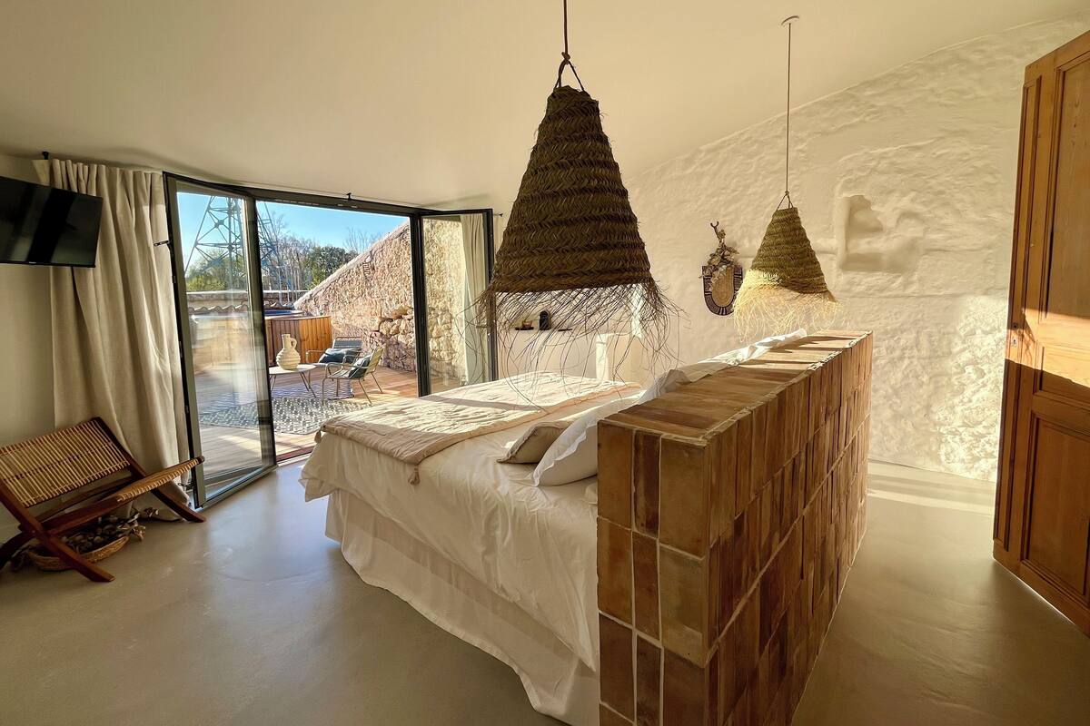 Een moderne slaapkamer met een groot bed, een houten hoofdbord, een aan de muur bevestigde televisie en een uitzicht buiten via een schuifdeur.