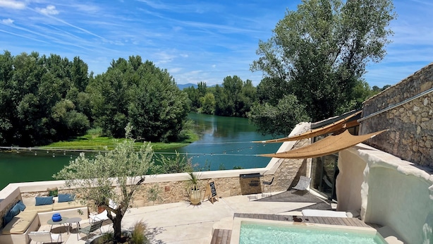 Un espace piscine sur le toit, offrant une vue sur un lac, avec des sièges extérieurs et un mur en pierre.