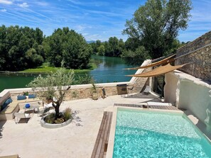 Un espace piscine sur le toit, offrant une vue sur un lac, avec des sièges extérieurs et un mur en pierre.
