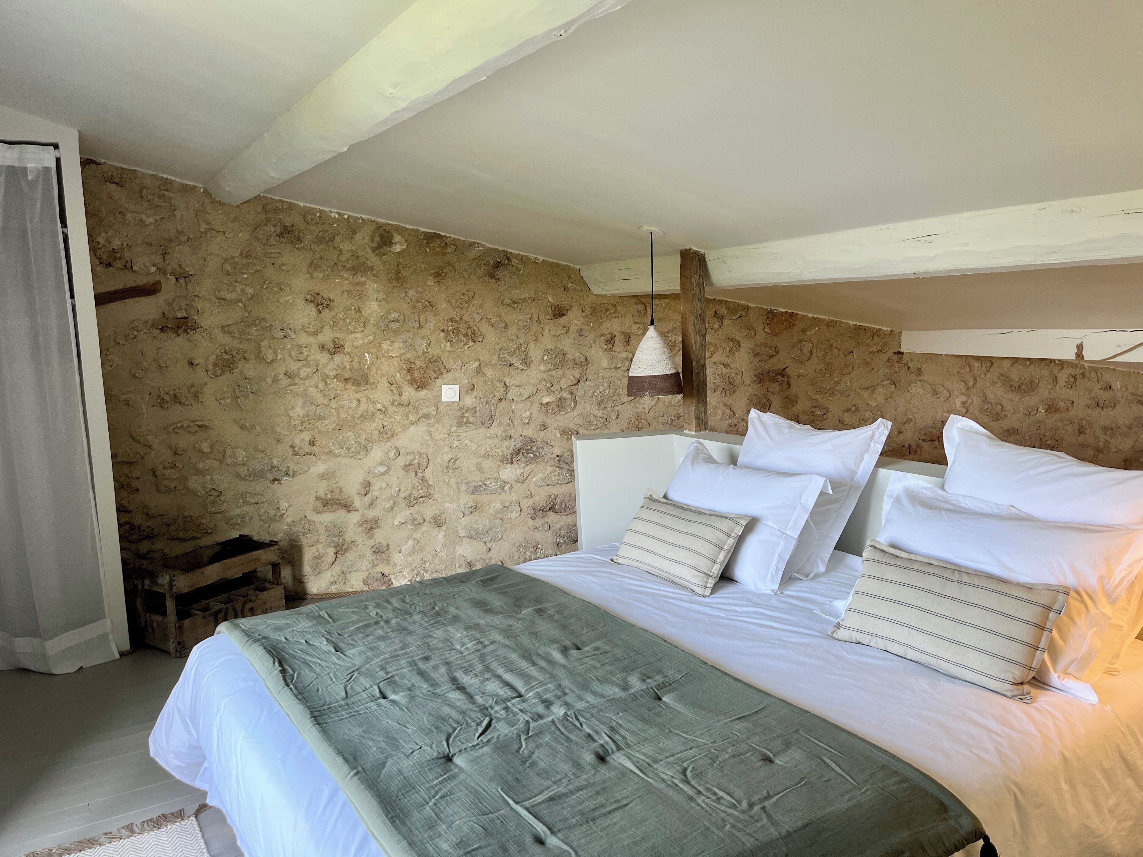 A bedroom with a stone wall, a wooden headboard, a bed with white bedding, and a hanging light fixture.