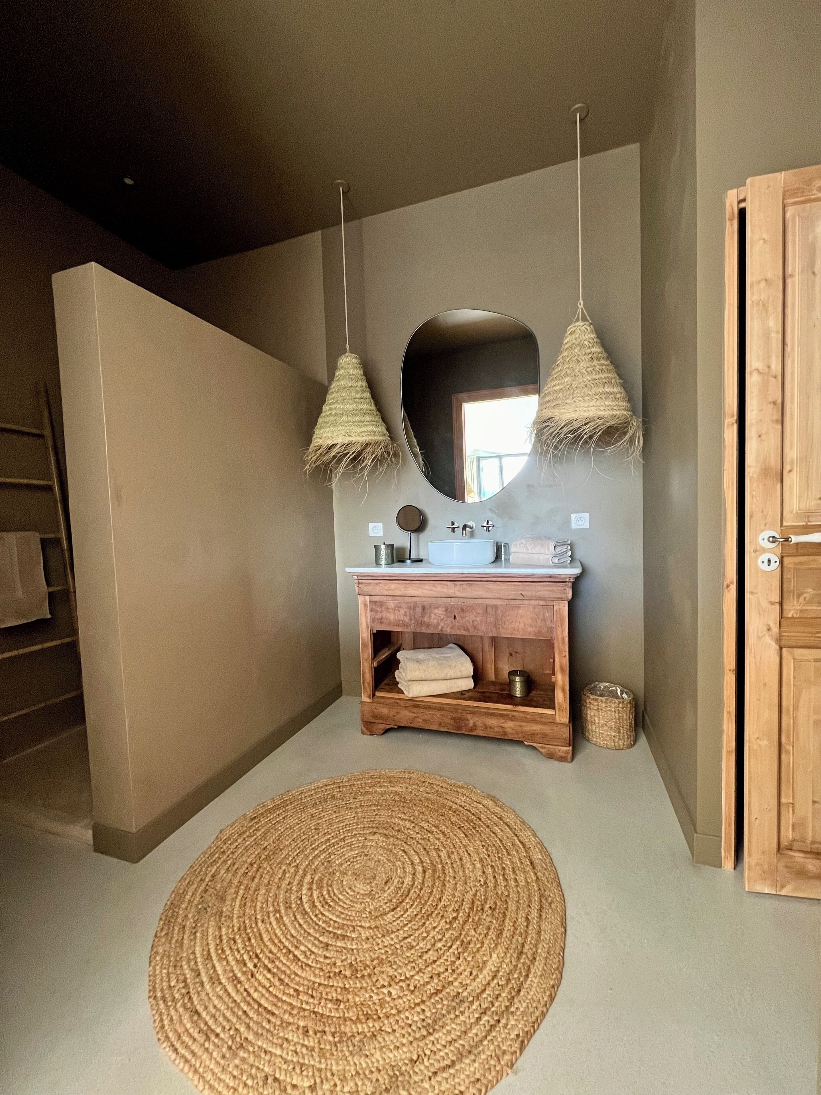 A bathroom with a wooden vanity, a round mirror, and two hanging light fixtures.