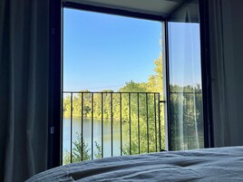 Un dormitorio con un ventanal grande con vistas a un lago y árboles.