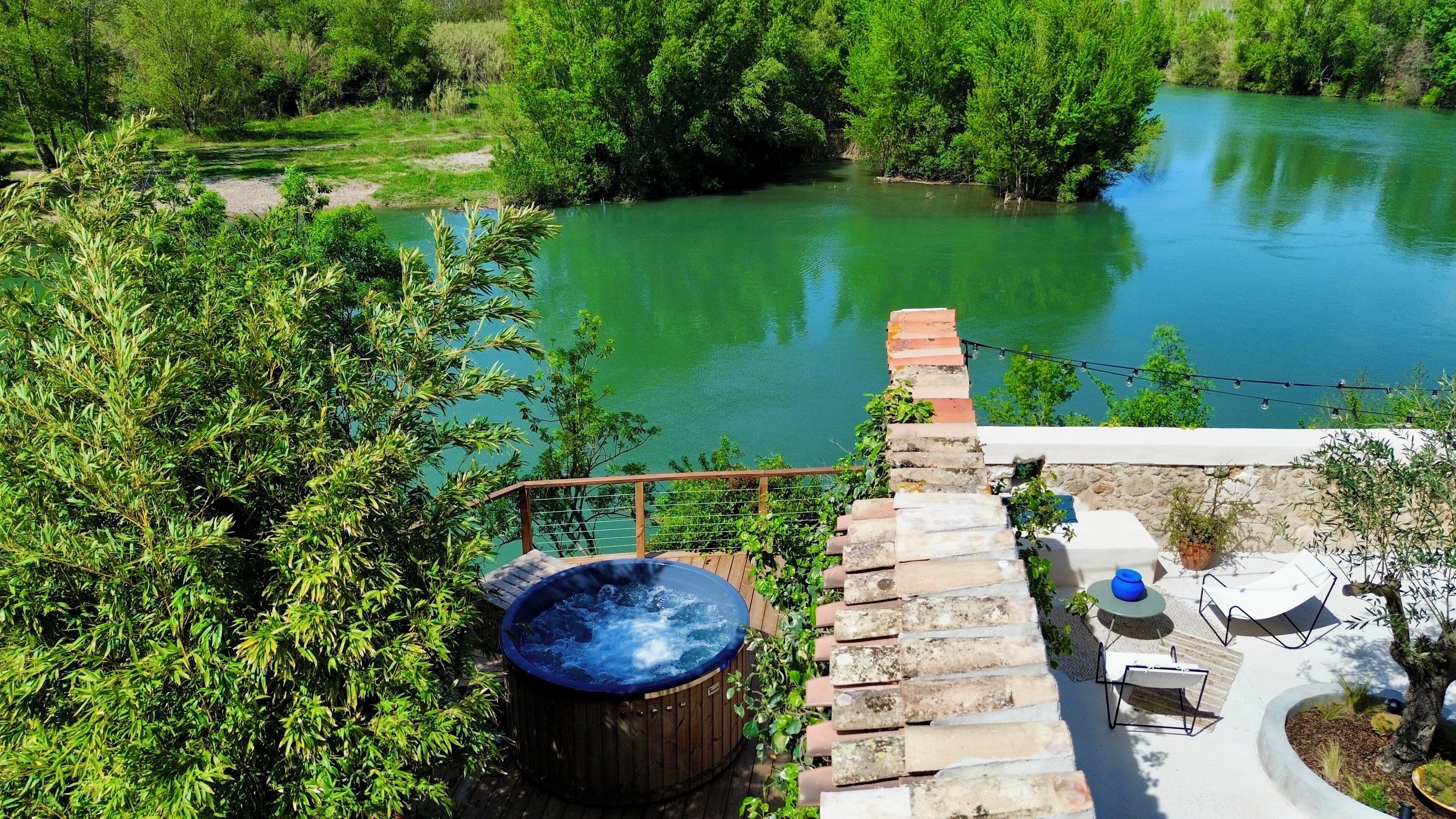 Un bain à remous sur une terrasse en bois avec vue sur la rivière.