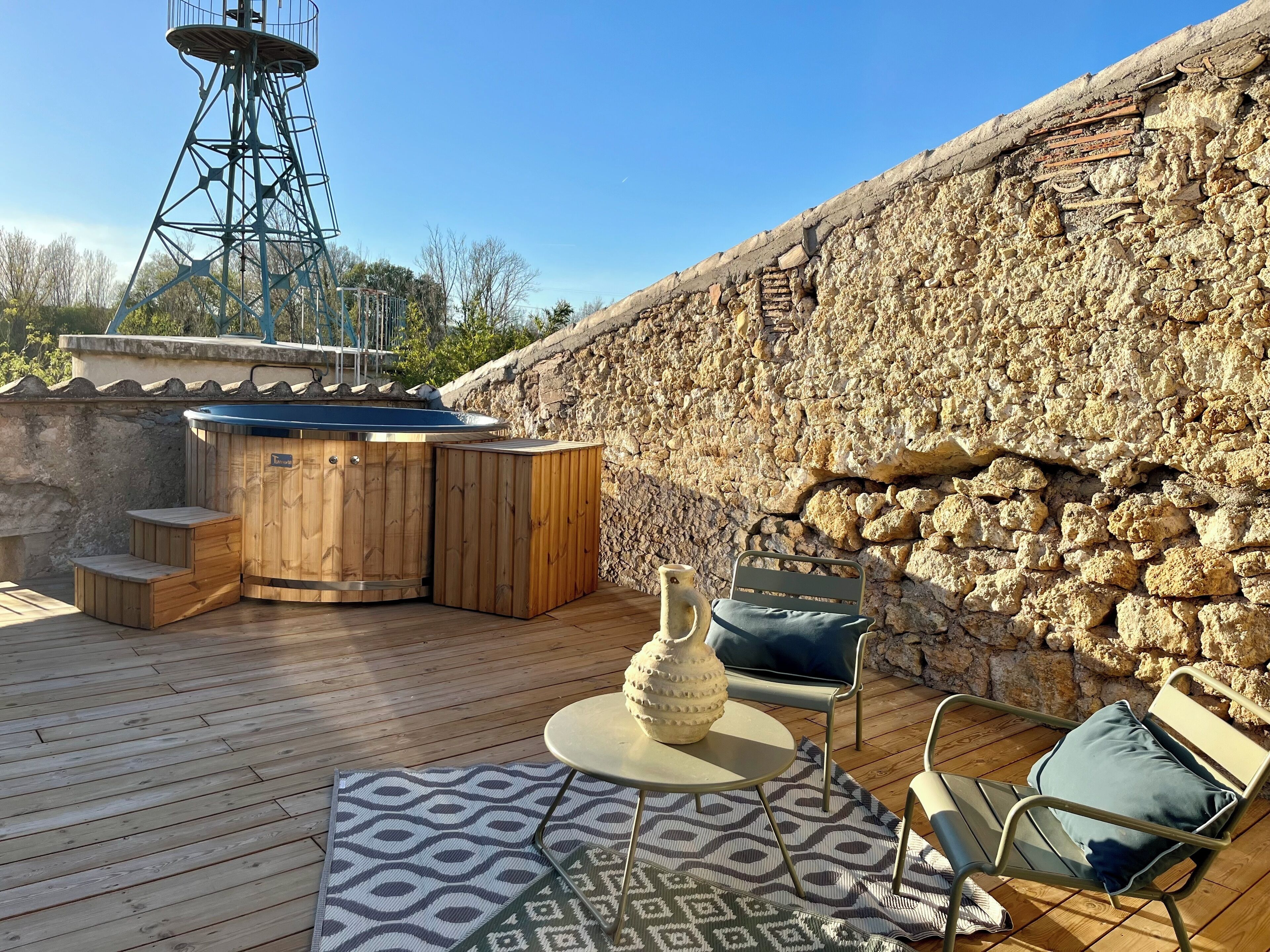 A wooden deck with a hot tub, outdoor seating, and a stone wall.