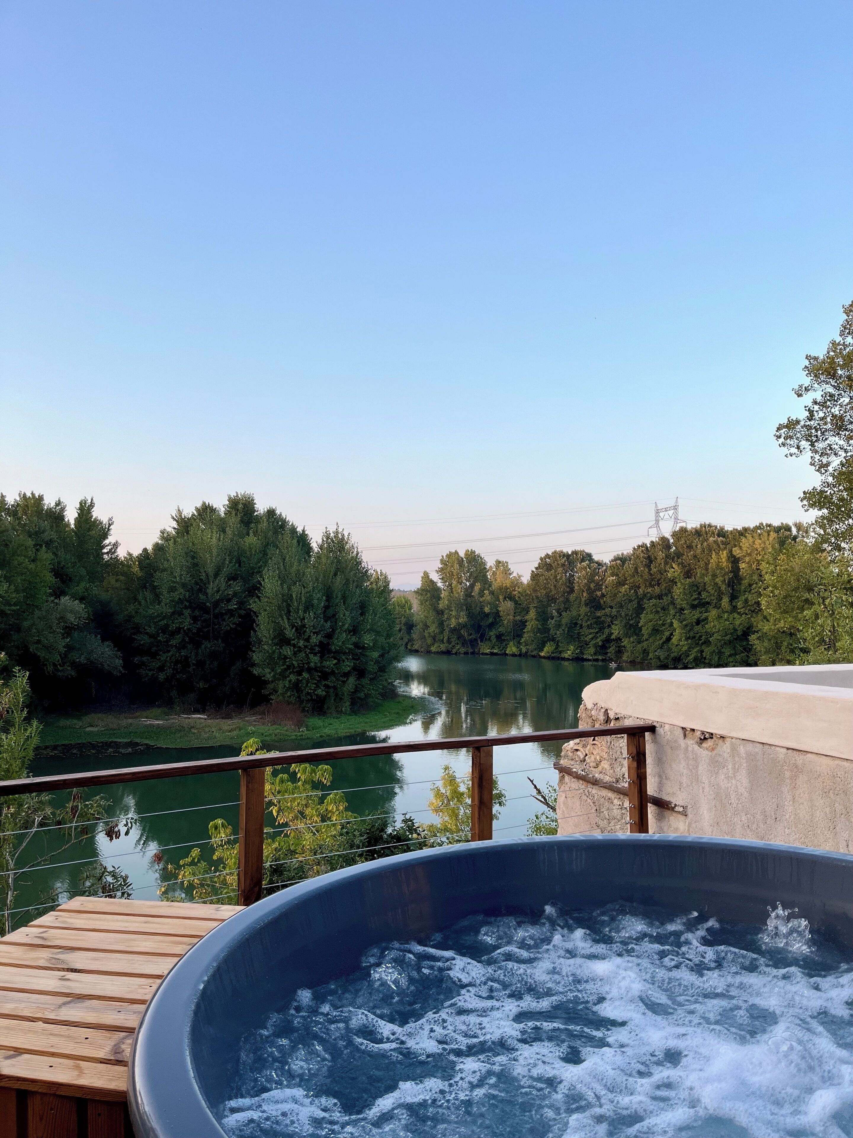 Un bain à remous sur une terrasse en bois, avec vue sur une rivière et des arbres.
