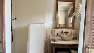 Uma casa de banho com chuveiro, lavatório com espelho e porta-toalhas.
