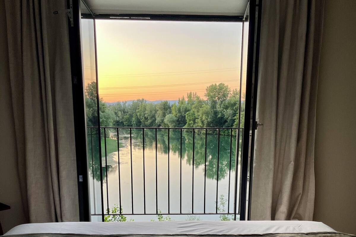 Een hotelkamer met een bed, uitzicht op een rivier en een balkon met een hekwerk.