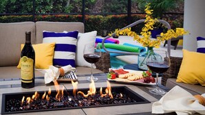 A cozy outdoor seating area with a fire feature, a bottle of wine, and a plate of food.