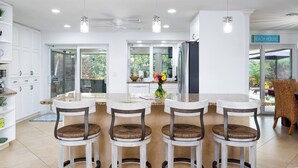 A modern kitchen with white cabinets, a central island with bar stools, and a view of the outdoors.