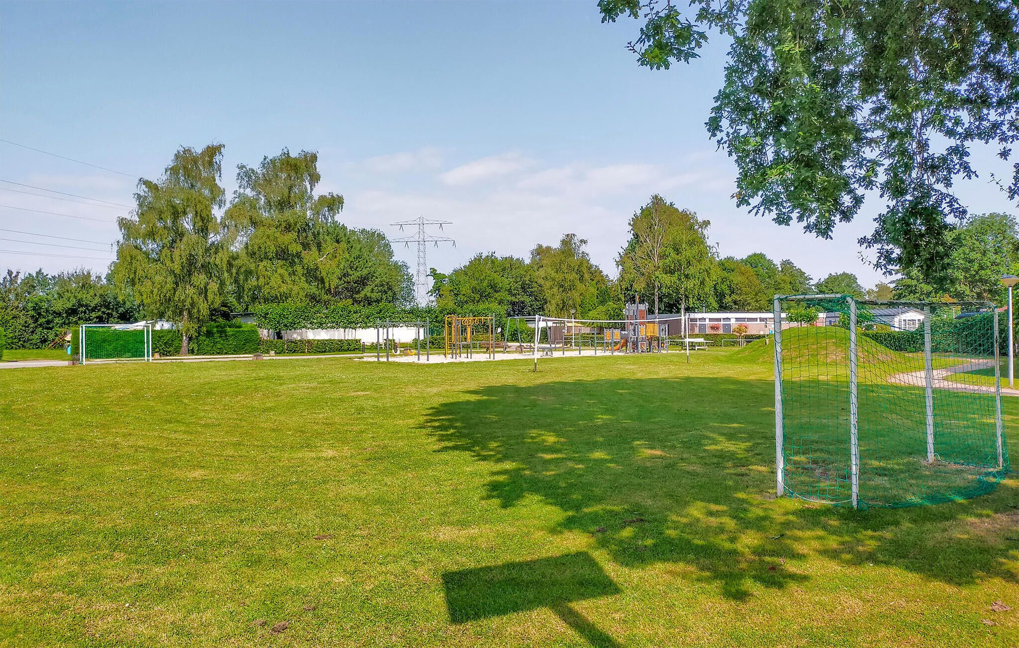 A grassy field with playground equipment, a goalpost, and trees in the background.