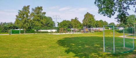 A grassy field with playground equipment, a goalpost, and trees in the background.