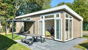 Ein modernes Haus mit einer Terrassenfläche, inklusive Tisch und Stühlen, sowie einem überdachten Sitzbereich.
