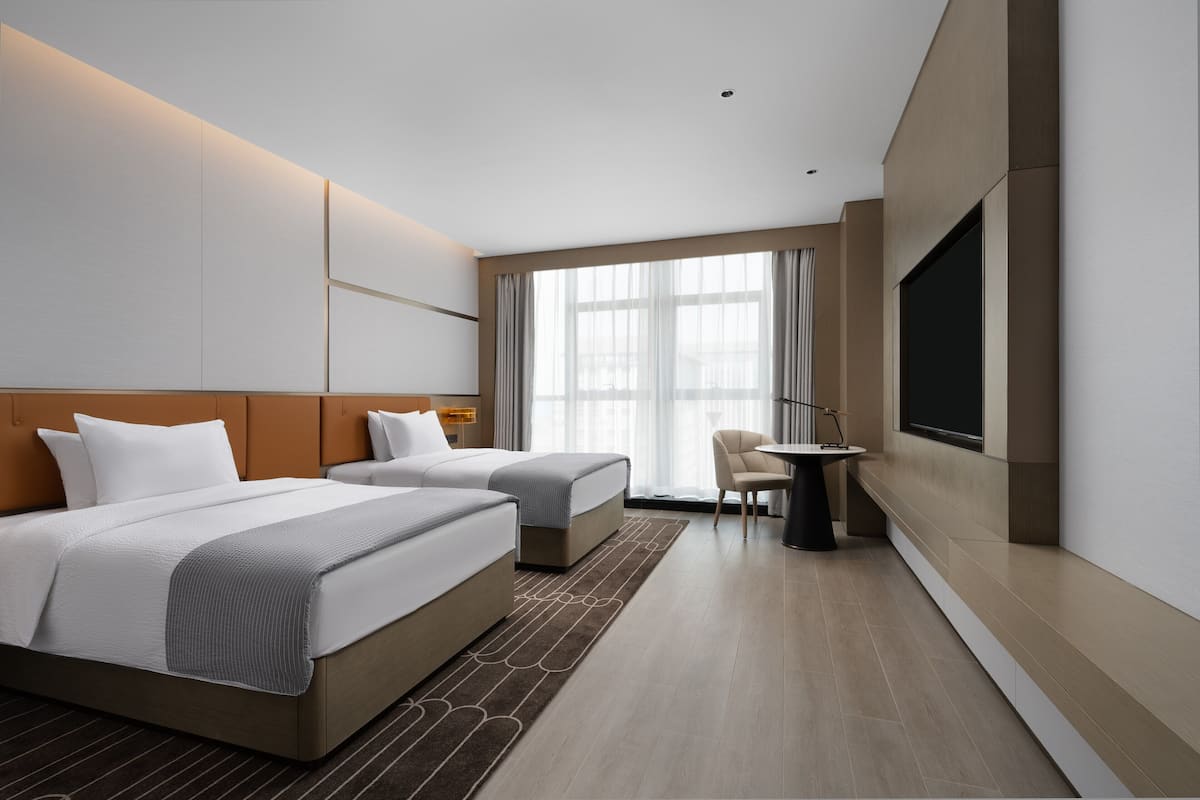 Una habitación de hotel moderna con dos camas, un escritorio y un televisor.